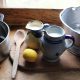 two jugs of milk, a lemon, a wooden spoon, a pot and a sieve with a dish towel - ingredients for how to make cream cheesem
