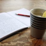 cup with hot lemon eater and open journal with writing and pen - morning routine