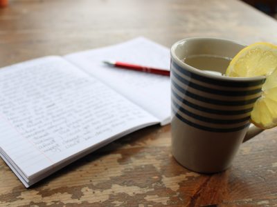 cup with hot lemon eater and open journal with writing and pen - morning routine