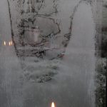 lit candle in front of icy window