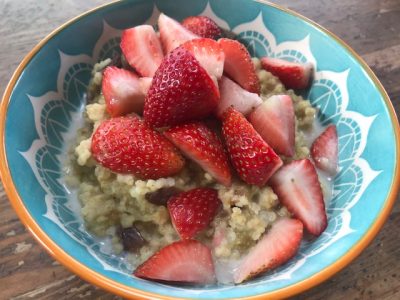 bowl with rhubarb millet porridge and freshly cut strawberries on top