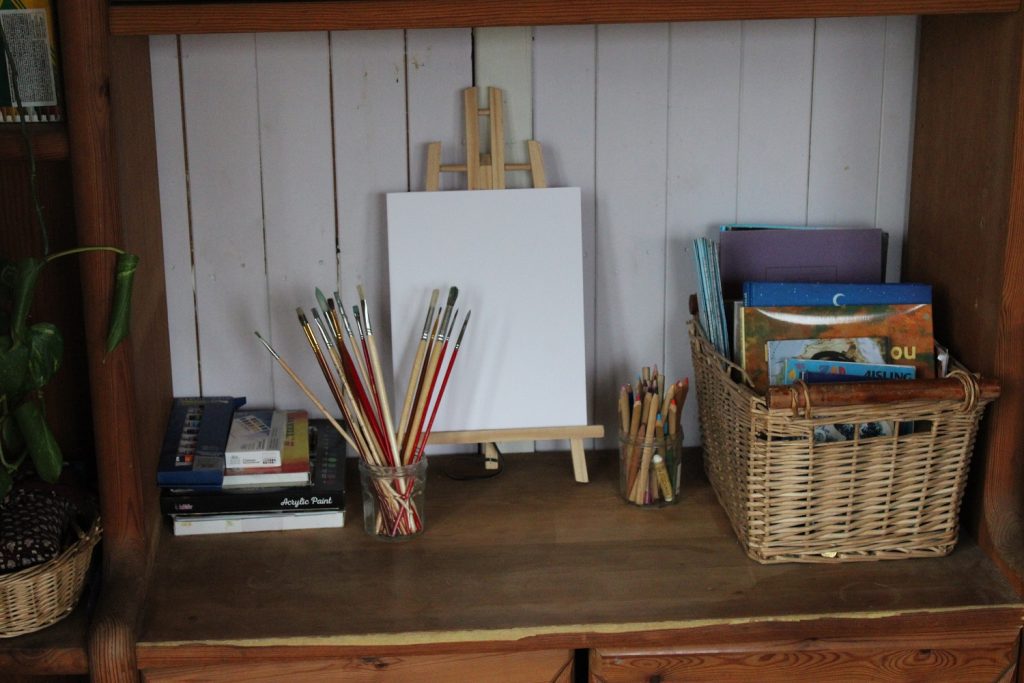 a more organized shelf for creativity: easel and art supplies, paint brushes, basket with books