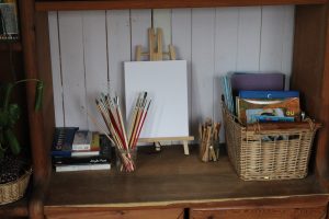 easel and art supplies, paint brushes, basket with books