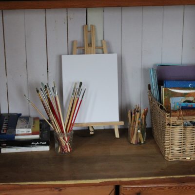 easel and art supplies, paint brushes, basket with books