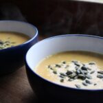 two bowls of carrot soup with pumpkin seeds