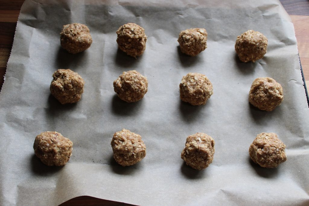 twelve balls of cookie dough on parchment paper before they are being flattened