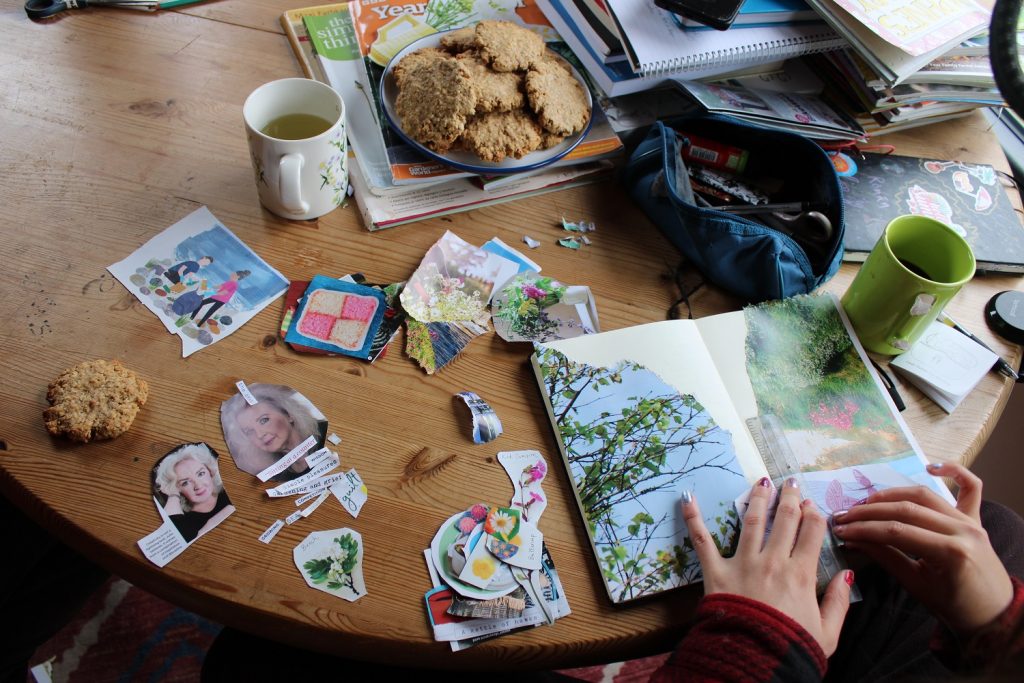female hands making a paper collage in a journal, a plate of biscuits and a cup of tea