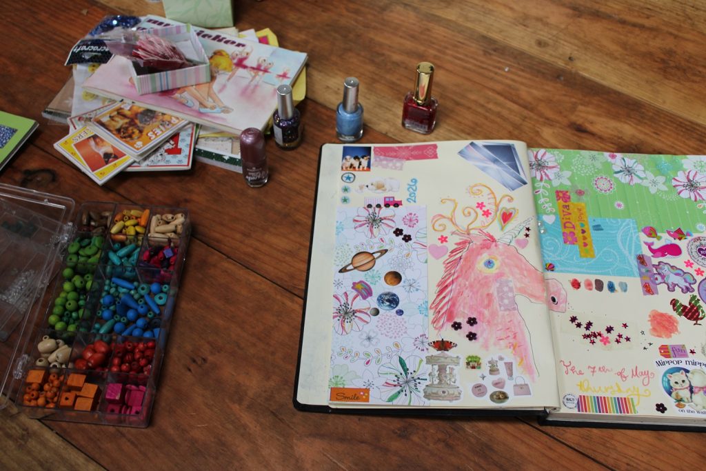 open sketchbook on floor, box of colourful beads, nail polish and stickers